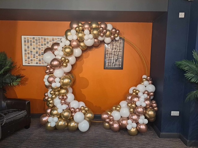 Black and gold balloon arch display with white accents indoors