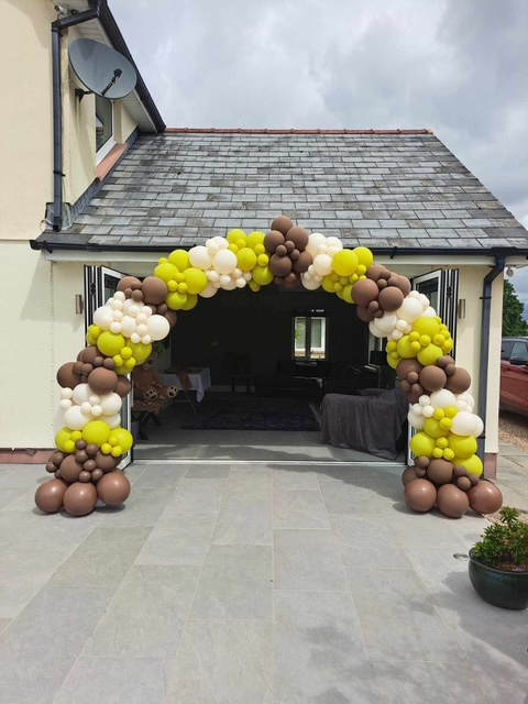 White, yellow and black balloon arch at an outdoor entrance